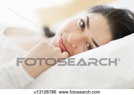 Stock Photograph - Portrait of young woman lying in bed. Fotosearch