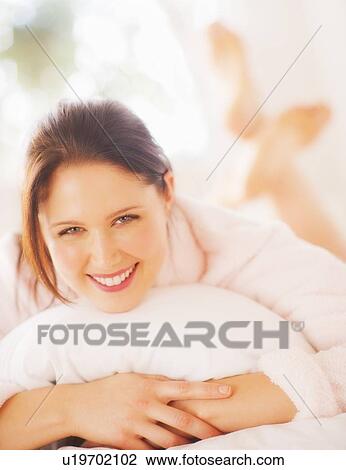 Stock Image - Portrait of young woman lying on bed. Fotosearch