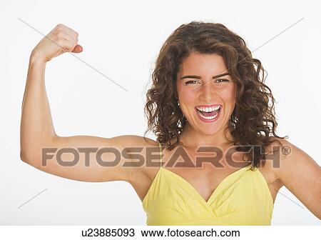 Stock Image - Portrait of young woman showing her biceps, studio shot. Fotosearch
