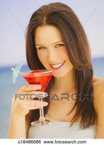 Stock Photograph - Portrait of young woman with cocktail, studio shot. Fotosearch