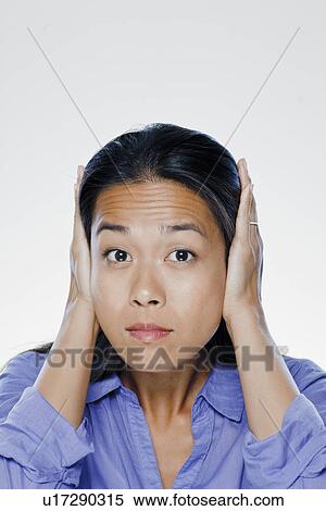 Stock Photography - Portrait of young woman with hands covering ears, studio shot. Fotosearch