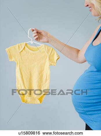 Stock Photograph - Pregnant woman holding onesie. Fotosearch