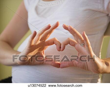 Stock Image - Pregnant woman making heart shape with hands. Fotosearch