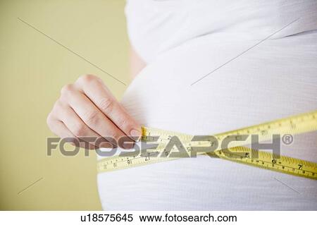 Stock Photography - Pregnant woman measuring belly with tape measure. Fotosearch