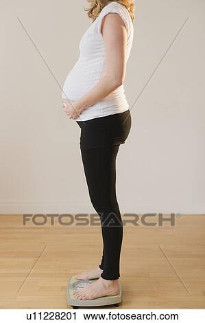 Stock Image - pregnant woman standing on weight scale. Fotosearch