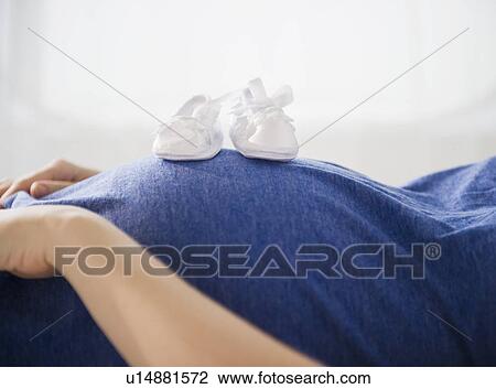 Stock Image - Pregnant woman with baby boots on belly. Fotosearch