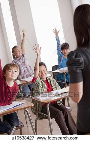Stock Photo - Pupils in classroom raising hands. Fotosearch