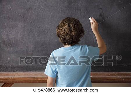 Stock Photograph - Rear view of schoolboy (10-11) writing on blackboard. Fotosearch