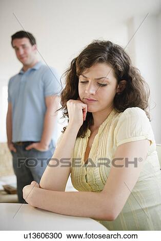 Sad woman sitting at table, man in background View Large Photo Image Stock Image - Sad woman sitting at table, man in background. Fotosearch