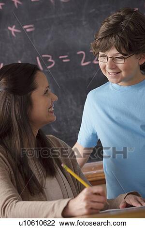 Stock Image - Schoolboy (10-11) and teacher face to face with blackboard in background. Fotosearch