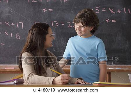 Stock Photo - Schoolboy (10-11) and teacher face to face with blackboard in background. Fotosearch