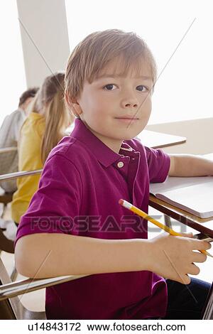 Stock Image - Schoolboy holding pencil in classroom. Fotosearch