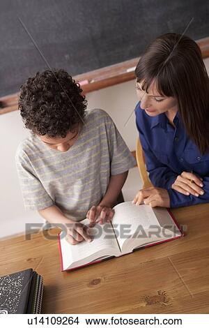 Picture - Schoolboy reading with teacher in classroom. Fotosearch