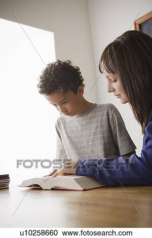 Stock Image - Schoolboy reading with teacher in classroom. Fotosearch