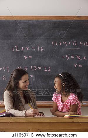 Stock Image - Schoolgirl (10-11) and teacher face to face with blackboard in background. Fotosearch