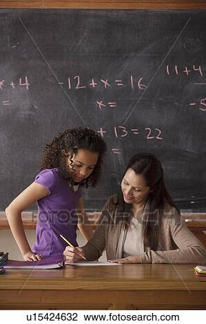 Stock Image - Schoolgirl (10-11) and teacher with blackboard in background. Fotosearch