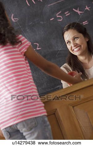Stock Photo - Schoolgirl (10-11) giving apple to his teacher. Fotosearch