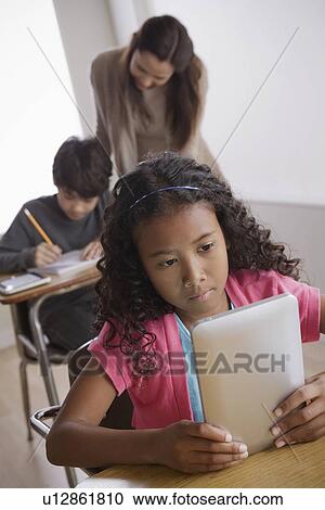 Schoolgirl (10-11) holding digital tablet with boy (12-13) and teacher in background View Large Photo Image Stock Image - Schoolgirl (10-11) holding digital tablet with boy (12-13) and teacher in background. Fotosearch