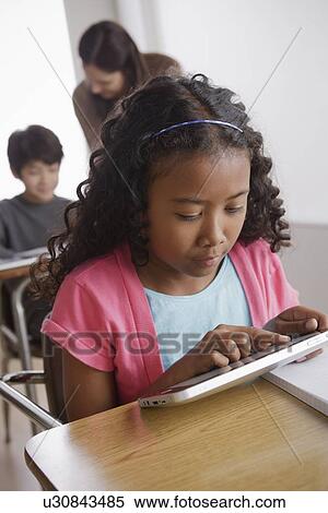 Schoolgirl (10-11) holding digital tablet with boy (12-13) and teacher in background View Large Photo Image Stock Photography - Schoolgirl (10-11) holding digital tablet with boy (12-13) and teacher in background. Fotosearch