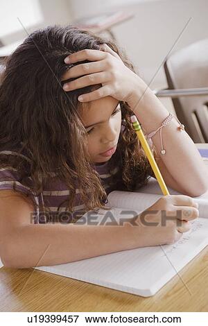 Stock Photo - Schoolgirl focused on writing in classroom. Fotosearch