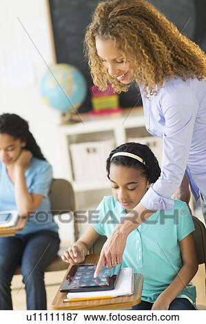 Stock Photo - Schoolgirls (10-13) using tablet pc, assisted by teacher. Fotosearch