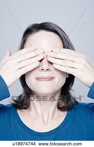 Picture - Smiling mid adult woman with hands covering eyes, studio shot. Fotosearch