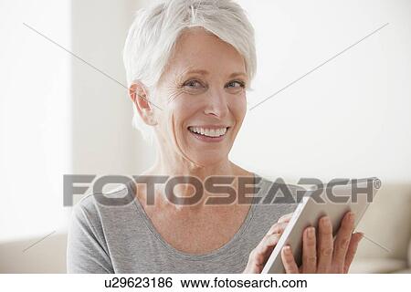 Stock Photograph - Smiling senior woman using digital tablet. Fotosearch
