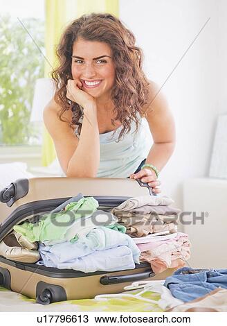 Stock Image - Smiling woman packing suitcase . Fotosearch