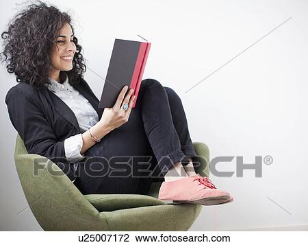 Stock Image - Studio shot of happy young woman reading book. Fotosearch