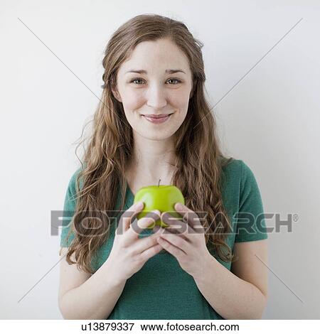 Studio shot of happy young woman holding green apple View Large Photo Image Stock Photo - Studio shot of happy young woman holding green apple. Fotosearch