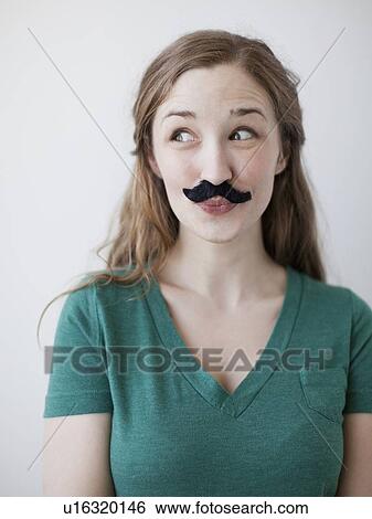 Stock Photograph - Studio shot of happy young woman with fake moustache. Fotosearch