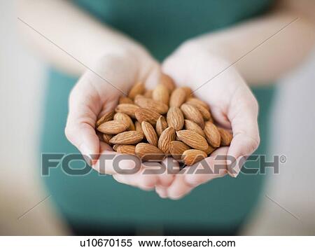 Stock Photography - Studio shot of woman showing handful of almonds. Fotosearch