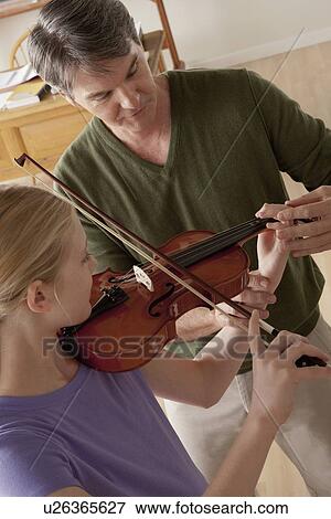 Stock Photo - Teacher showing to teenage girl (14-15) how to play violin. Fotosearch