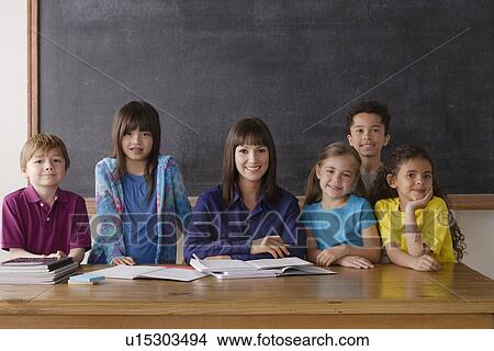 Picture - Teacher sitting by desk with group of pupils. Fotosearch