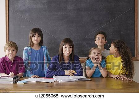 Teacher sitting by desk with group of pupils View Large Photo Image Stock Photography - Teacher sitting by desk with group of pupils. Fotosearch