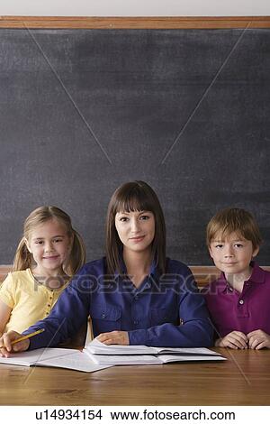 Teacher sitting by desk with two pupils View Large Photo Image Picture - Teacher sitting by desk with two pupils. Fotosearch