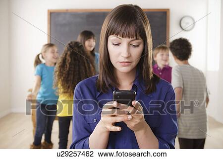 Stock Image - Teacher using mobile phone with group of pupils in background. Fotosearch