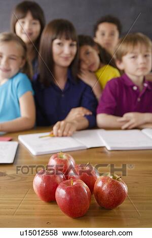 Stock Photo - Teacher with group of pupils and apples on desk. Fotosearch