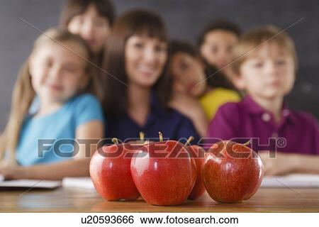 Stock Photograph - Teacher with group of pupils and apples on desk. Fotosearch