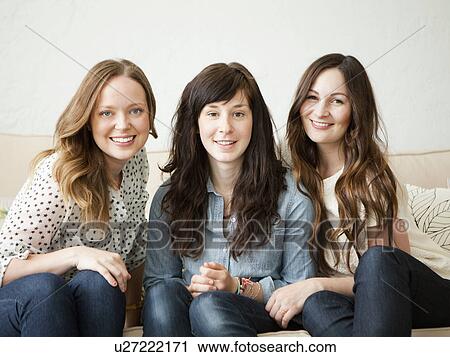 Stock Image - Three young female friends sitting on sofa. Fotosearch