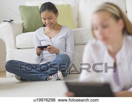 Two girls (14-17) relaxing at home using digital devices View Large Photo Image Stock Photo - Two girls (14-17) relaxing at home using digital devices. Fotosearch