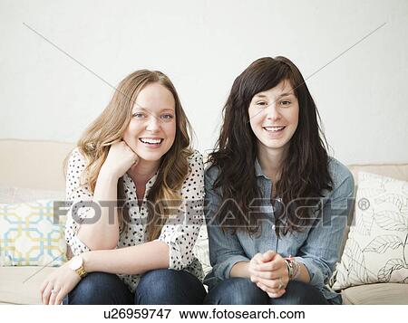 Two young female friends sitting on sofa View Large Photo Image Stock Photo - Two young female friends sitting on sofa. Fotosearch
