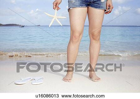 Stock Image - United States Virgin Islands, St. John, Woman on bench holding starfish. Fotosearch