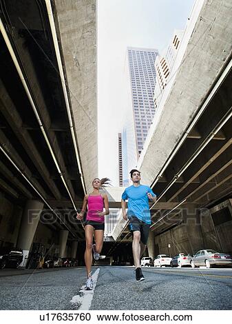 Stock Image - USA, California, Los Angeles, Young man and young woman running on city street. Fotosearch