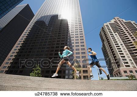 Stock Photo - USA, California, Los Angeles, Young man and young woman running in city. Fotosearch