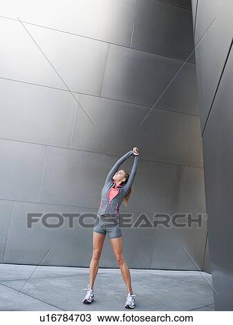 Stock Image - USA, California, Los Angeles, Young woman stretching near modern building. Fotosearch