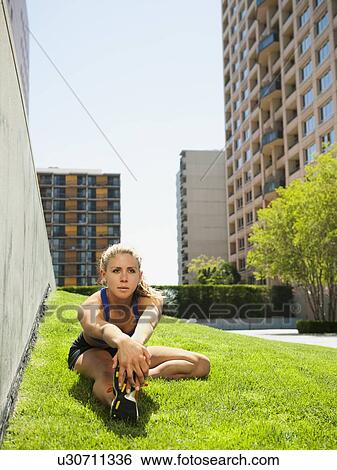 Stock Photograph - USA, California, Los Angeles, Young woman stretching on grass. Fotosearch