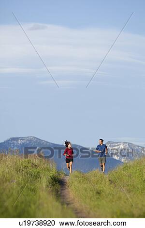 Stock Image - USA, Montana, Kalispell, Couple jogging in mountainside. Fotosearch
