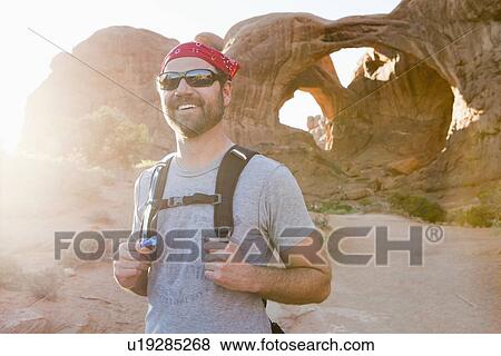 Stock Photo - USA, Utah, Moab, Mid adult man posing in front of natural arches. Fotosearch