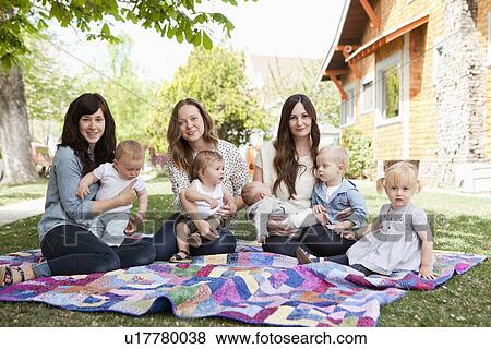 Stock Photo - USA, Utah, Salt Lake City, Three young mothers with two baby boys (6-11 months), toddler boy and girl (2-3) sitting in park. Fotosearch